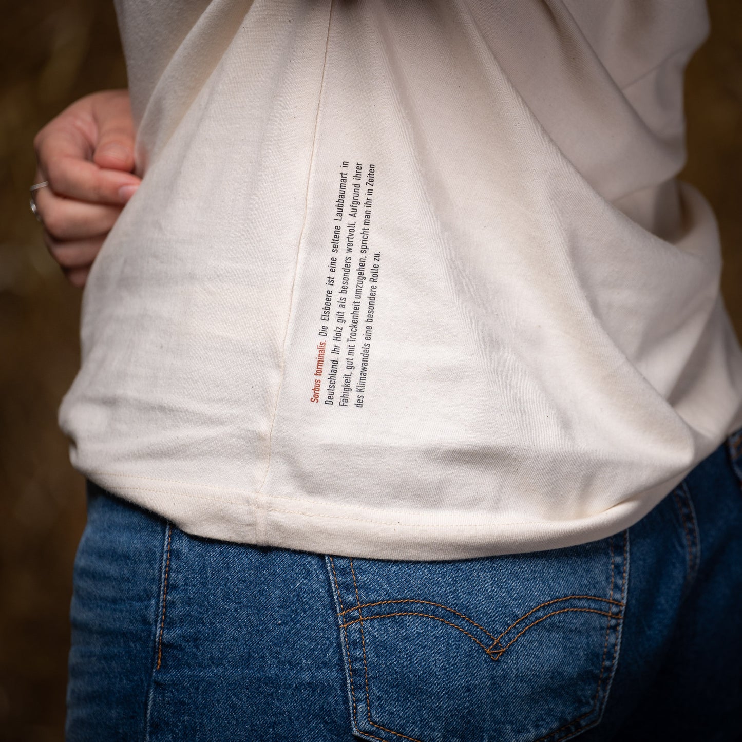 In dieser Nahaufnahme vom Waldshirt Elsbeere steht der Infotext zur Pflanze, der entlang der seitlichen Naht auf die Rückseite des Shirts gedruckt ist.