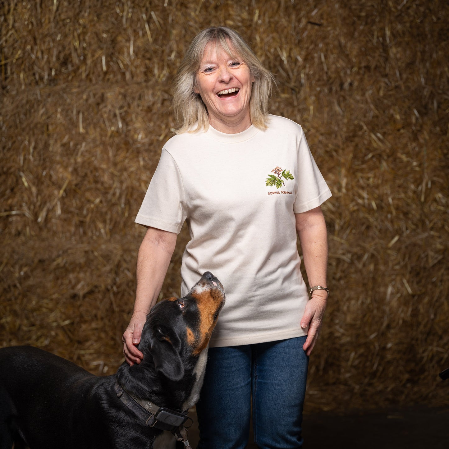 Susi trägt das Waldshirt Elsbeere in XS und streichelt dabei den großen schwarzen Hund Kurt. Kurt starrt fasziniert auf den Stick.