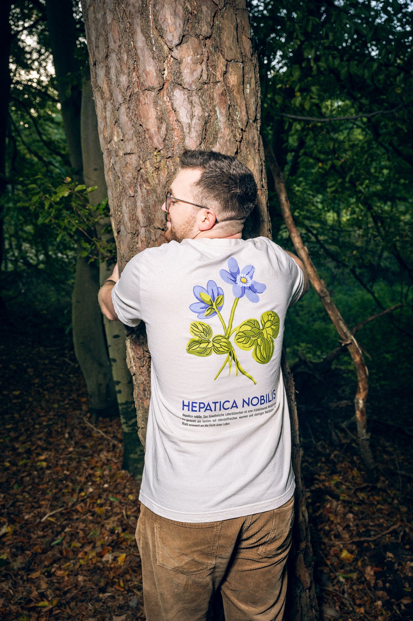 Felix im Waldshirt Leberblümchen. Man sieht ihn von hinten, wie er einen Baum umarmt.